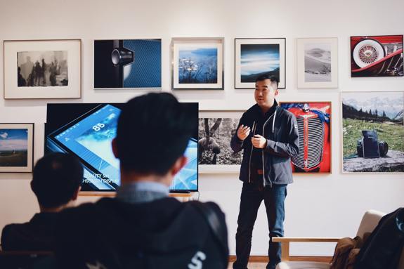 Man speaking to a crowd in front of wall of art. 